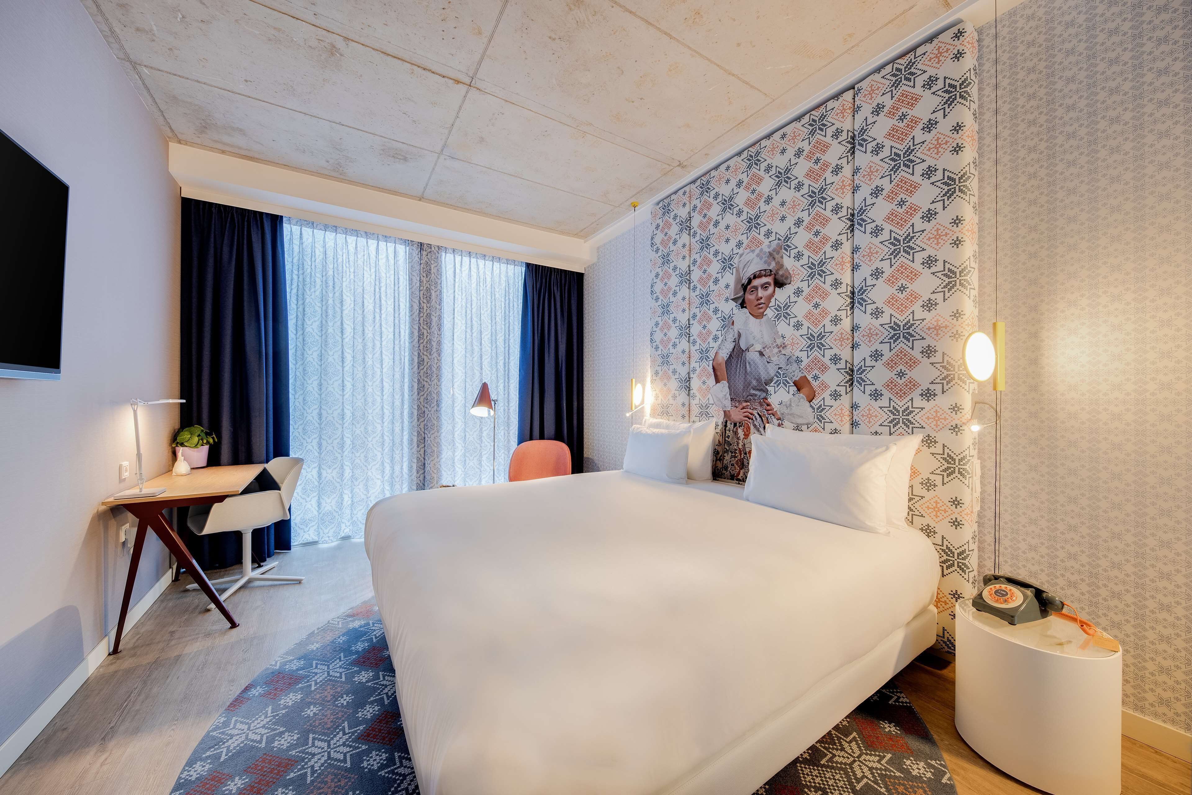 Hotelkamer met een groot bed, een bureau, een stoel, een televisie en een behang met patroon.