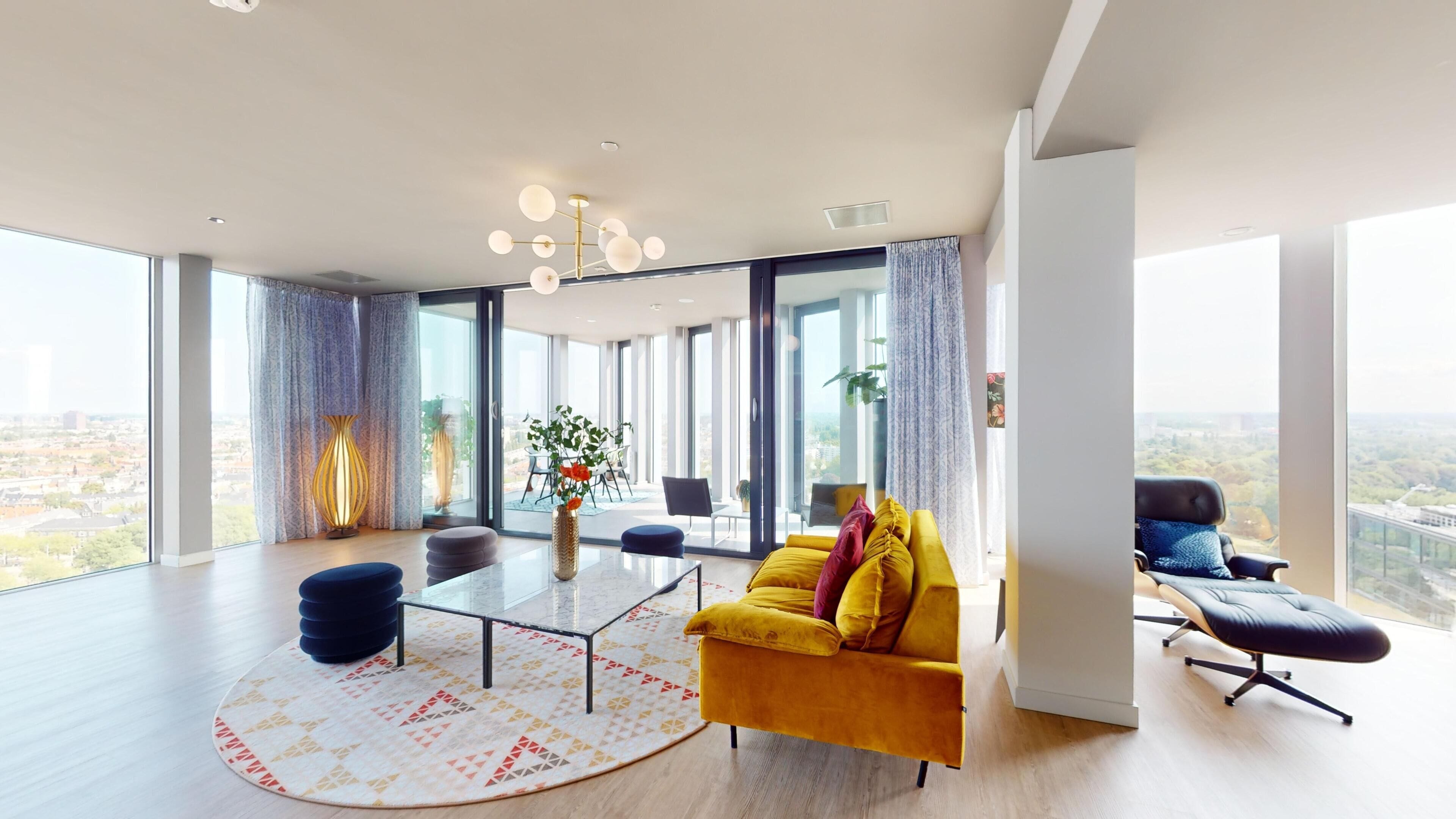 Een moderne woonkamer met een geel sofa, een glazen salontafel en een stadszicht door grote ramen.