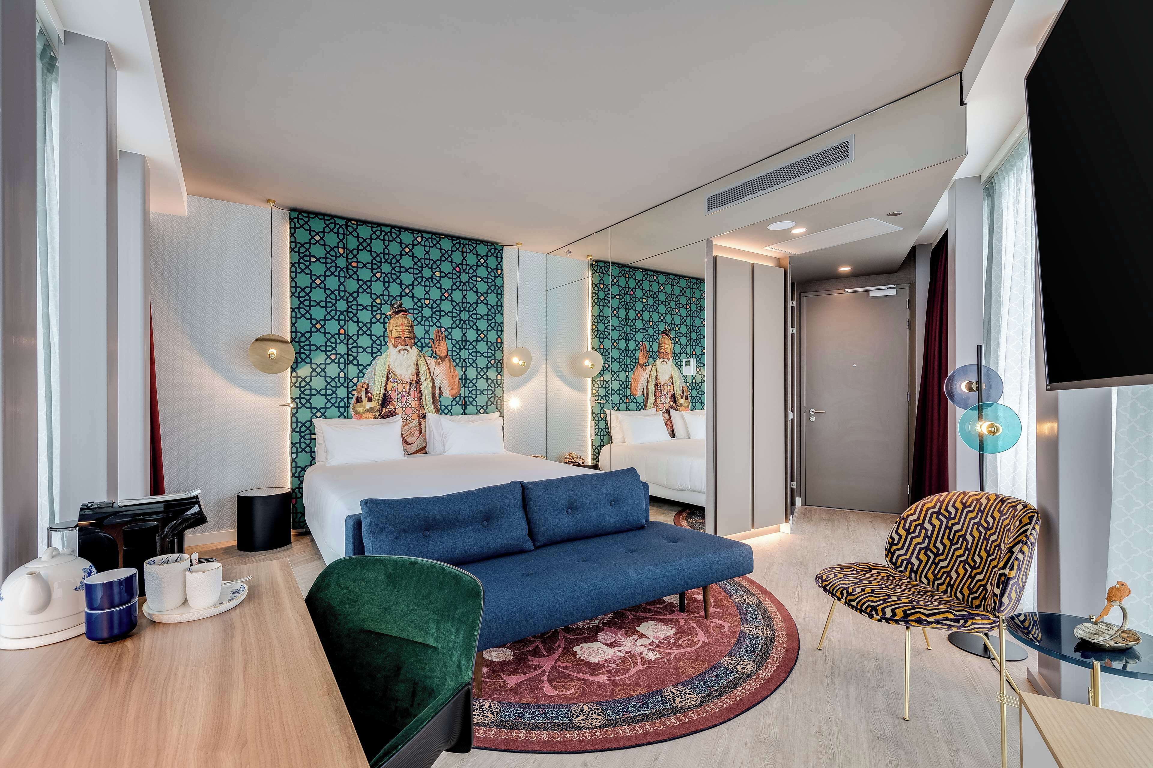 Una habitación de hotel moderna con una cama grande, un sofá azul, un papel tapiz estampado y una alfombra redonda.