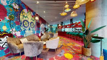 Um lobby vibrante com murais florais coloridos, assentos confortáveis e um bar.