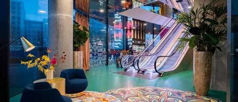 Un espacio interior moderno con un diseño de piso colorido, zonas de descanso y una escalera mecánica.