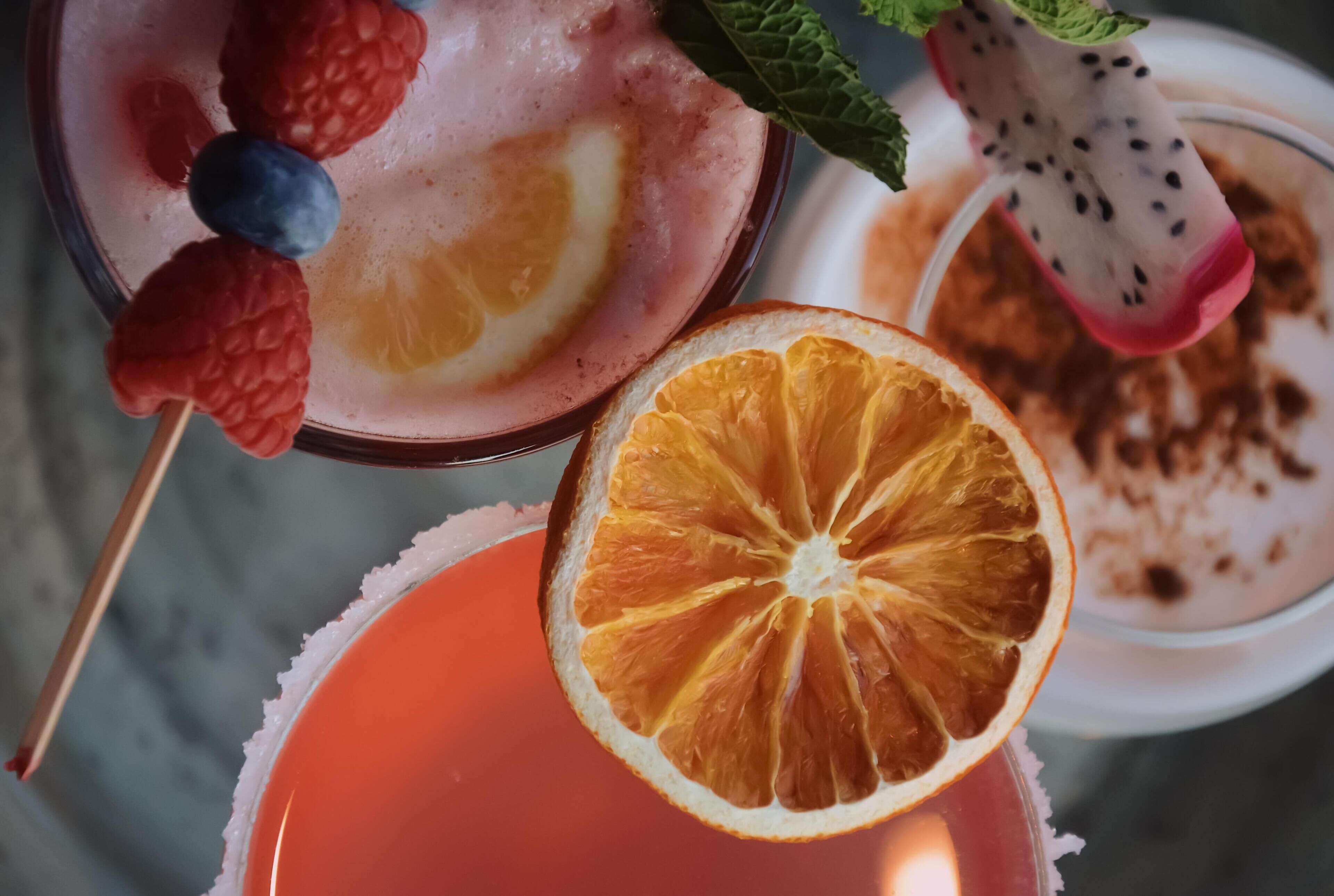Diverse fruitdranken, verrijkt met garnering zoals aardbeien, bosbessen en een sinaasappelschijf.