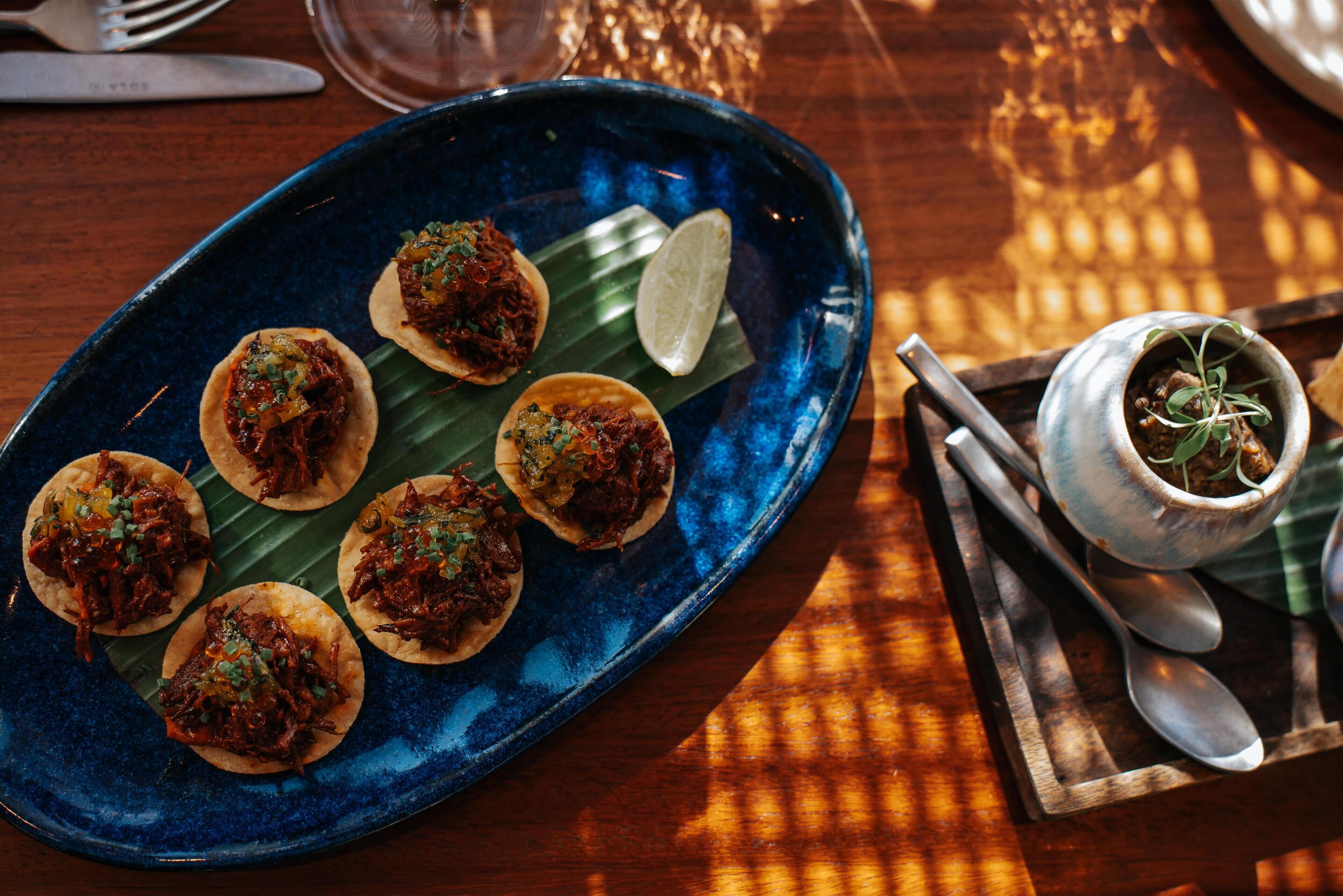 Ein blaues Teller mit Tacos auf einem Holztisch.