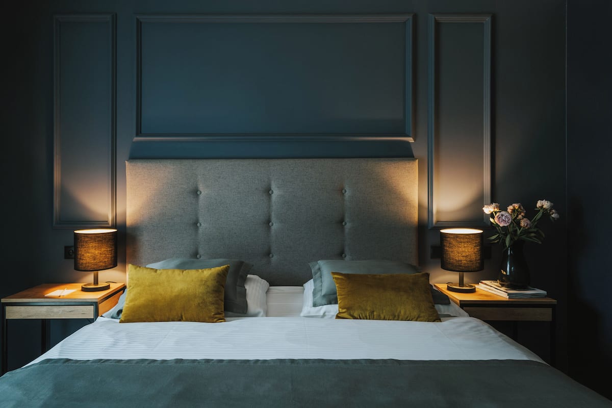 A neatly made bed with a tufted headboard, two bedside tables with lamps, and a vase with flowers on one table.