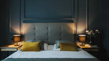 A neatly made bed with a tufted headboard, two bedside tables with lamps, and a vase with flowers on one table.