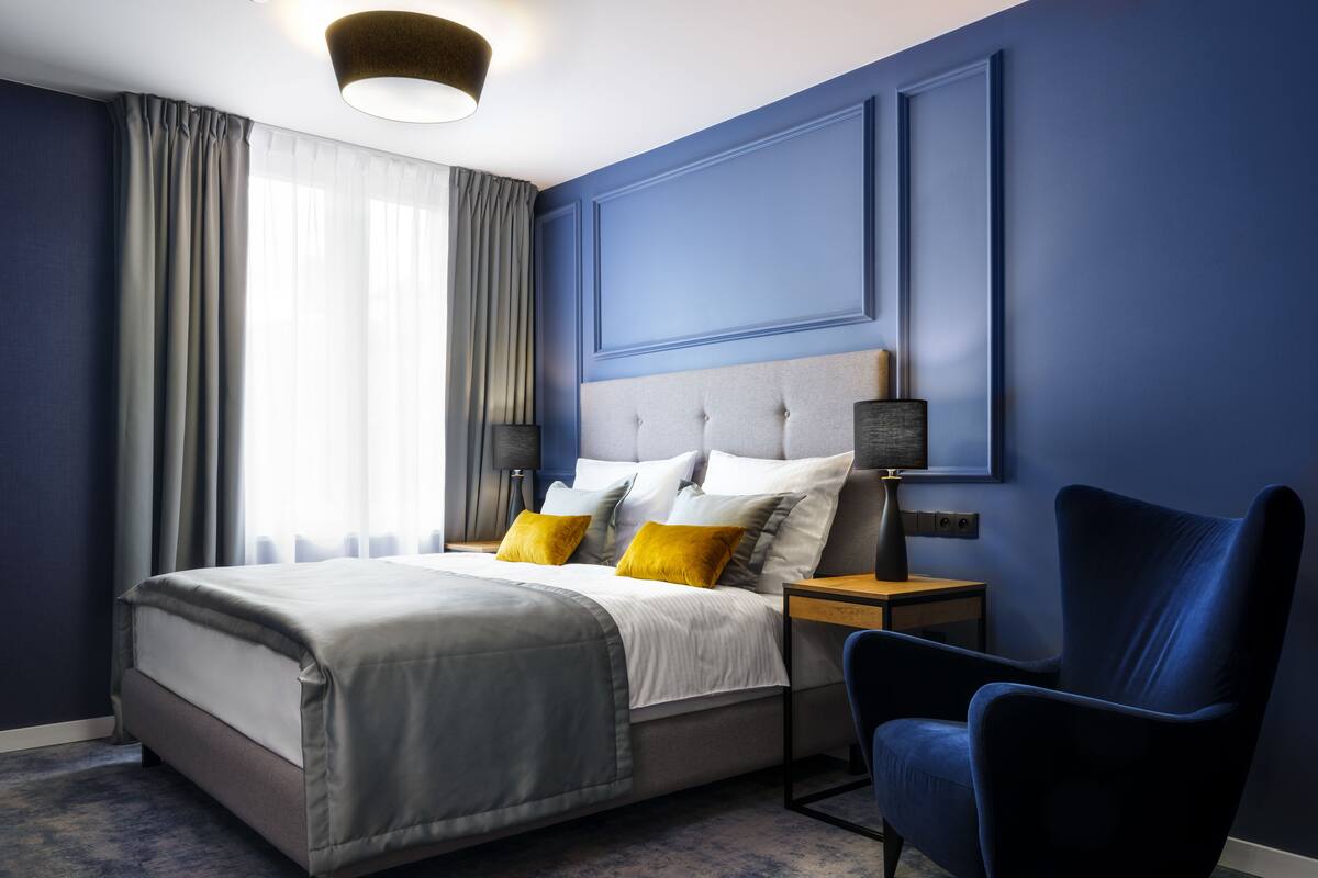 A modern bedroom with a bed, bedside tables, a chair, and a window with curtains.