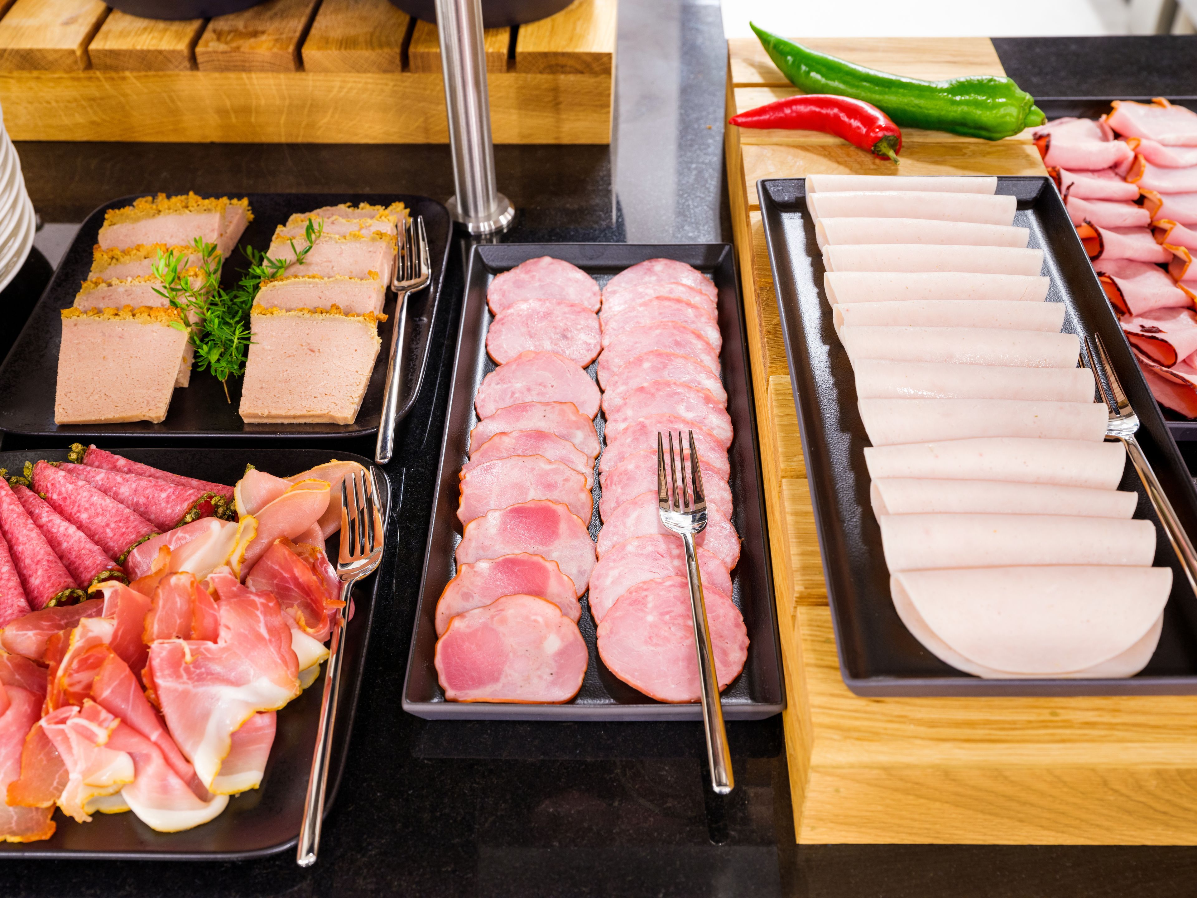 Buffet com diversos tipos de carnes fatiadas e queijos, incluindo presunto, fiambre e um patê.