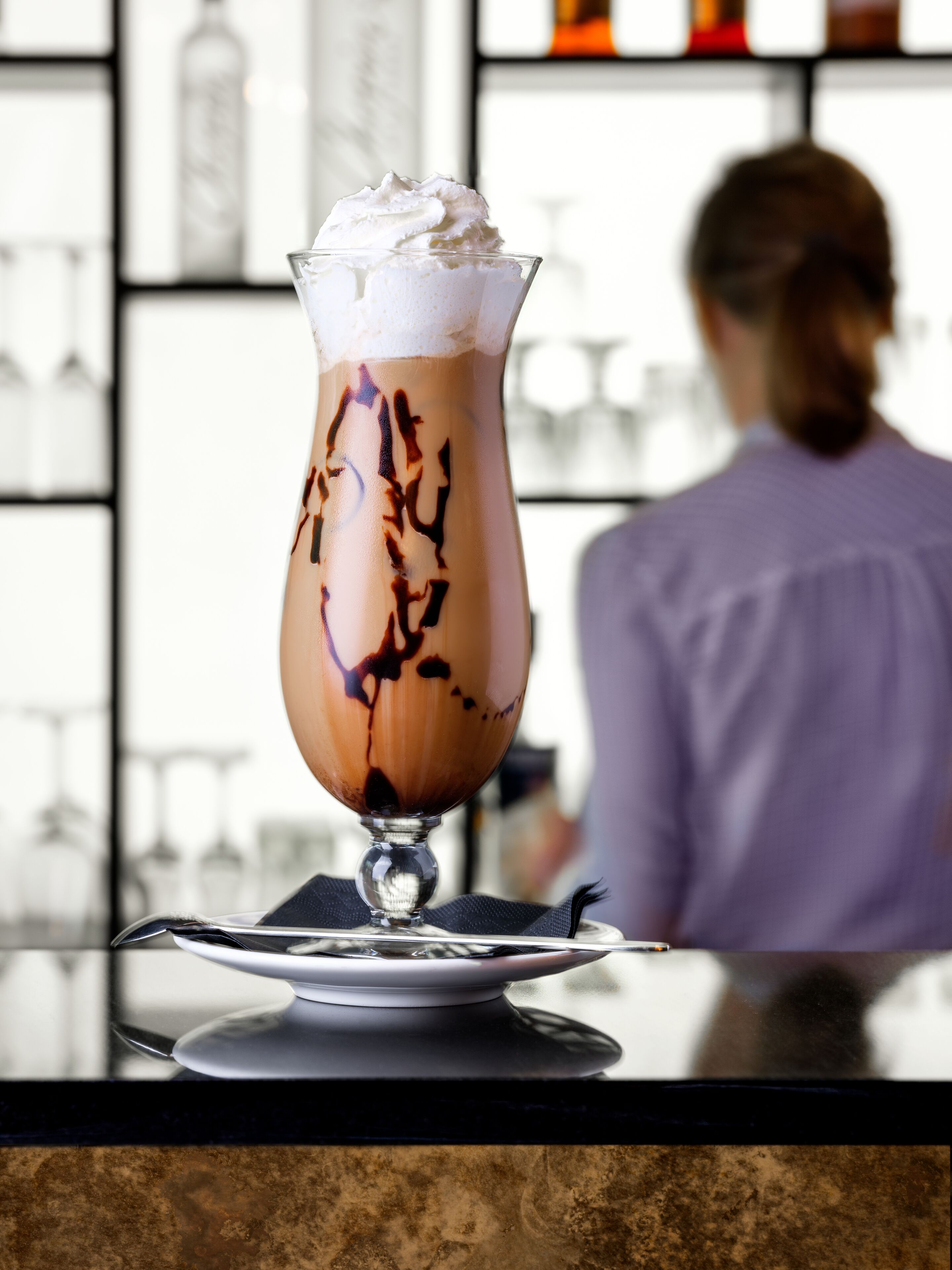 Un postre en vaso sobre una mesa, con un fondo difuso de una zona de bar.