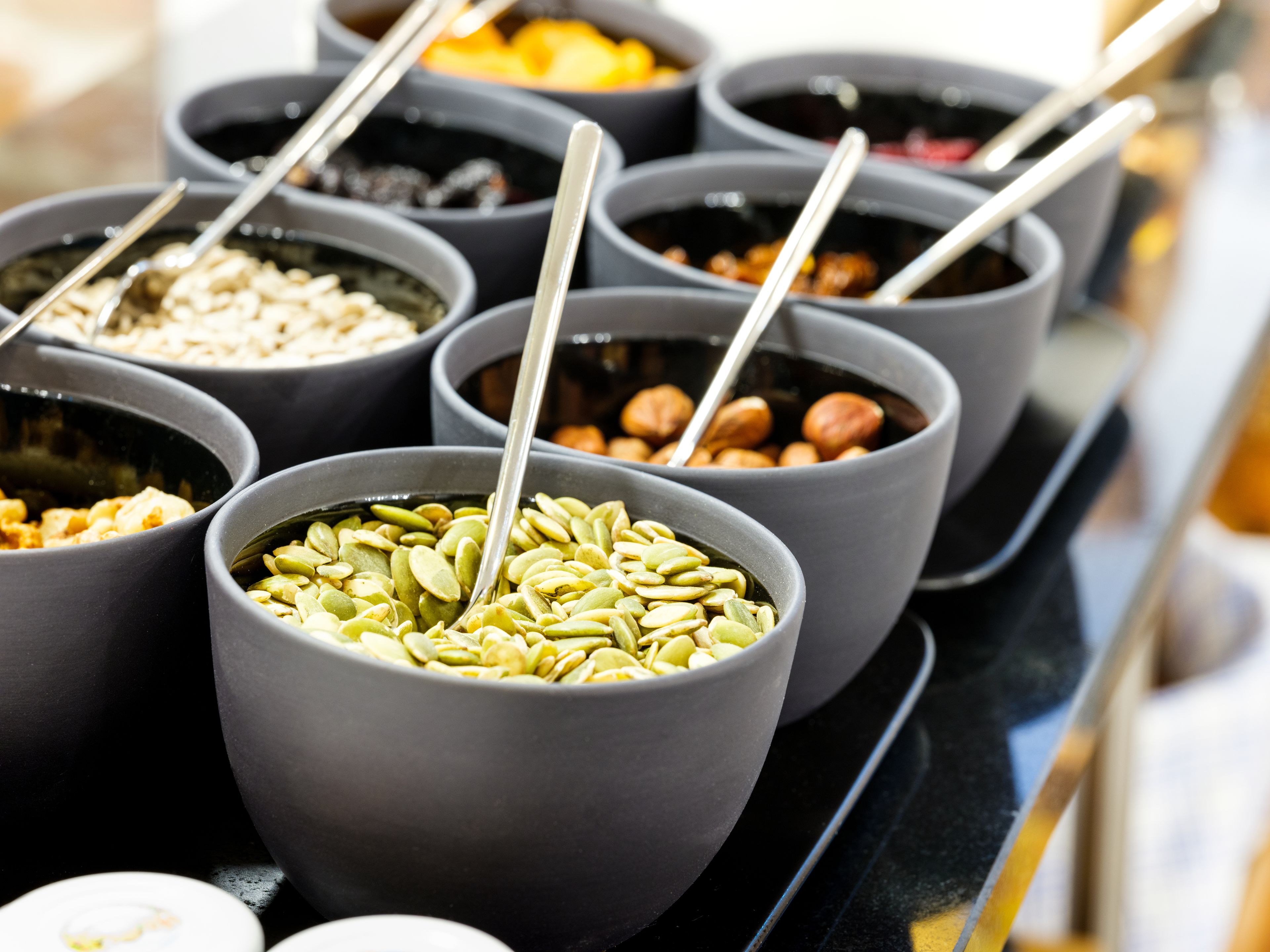 Une variété d’aliments servis dans des bols, accompagnés de cuillères, notamment des noix et des graines.