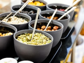 Diversos alimentos en cuencos con cucharas, como nueces y semillas.