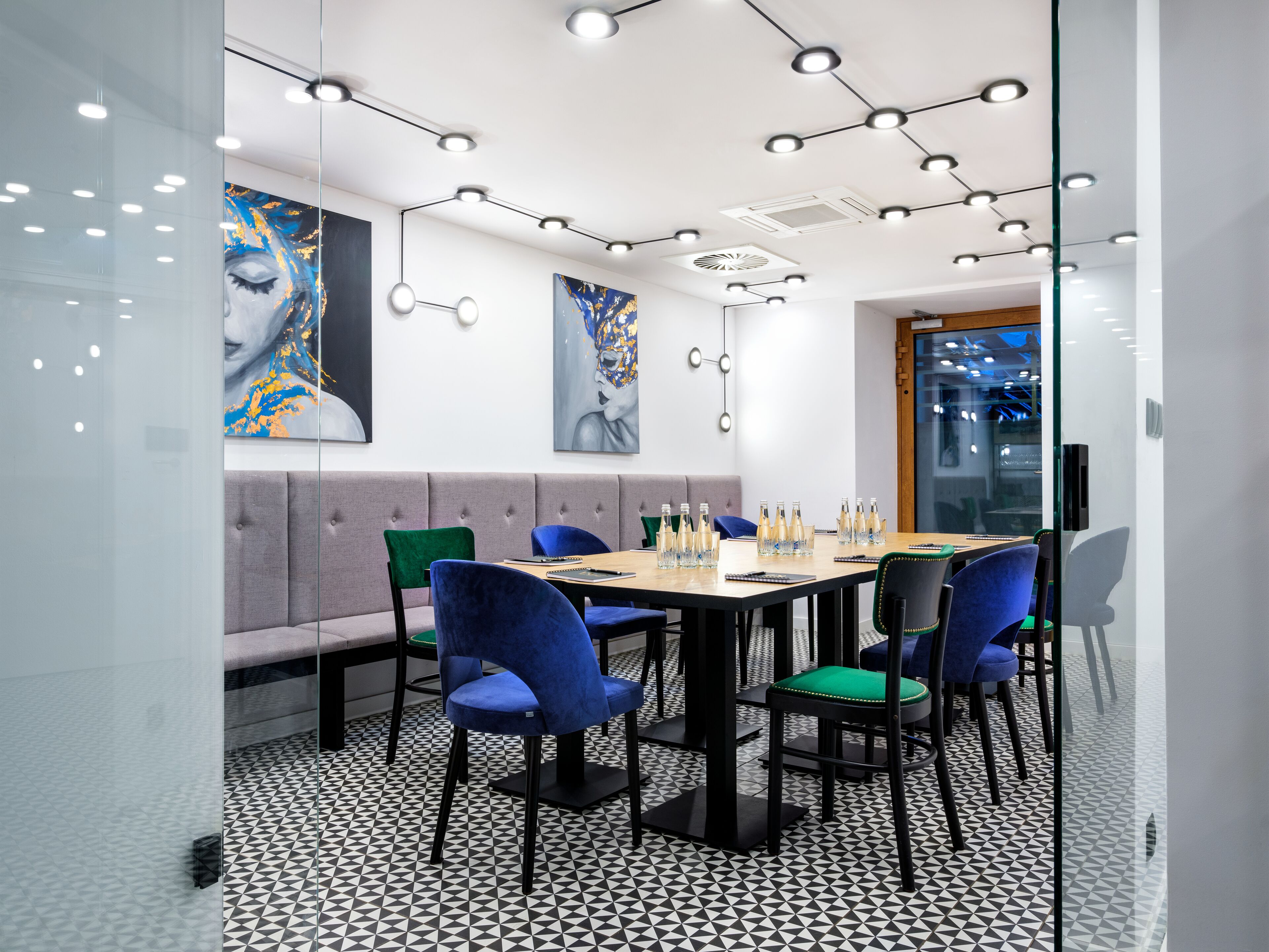 A modern meeting room with a glass partition, a round table, and blue chairs.