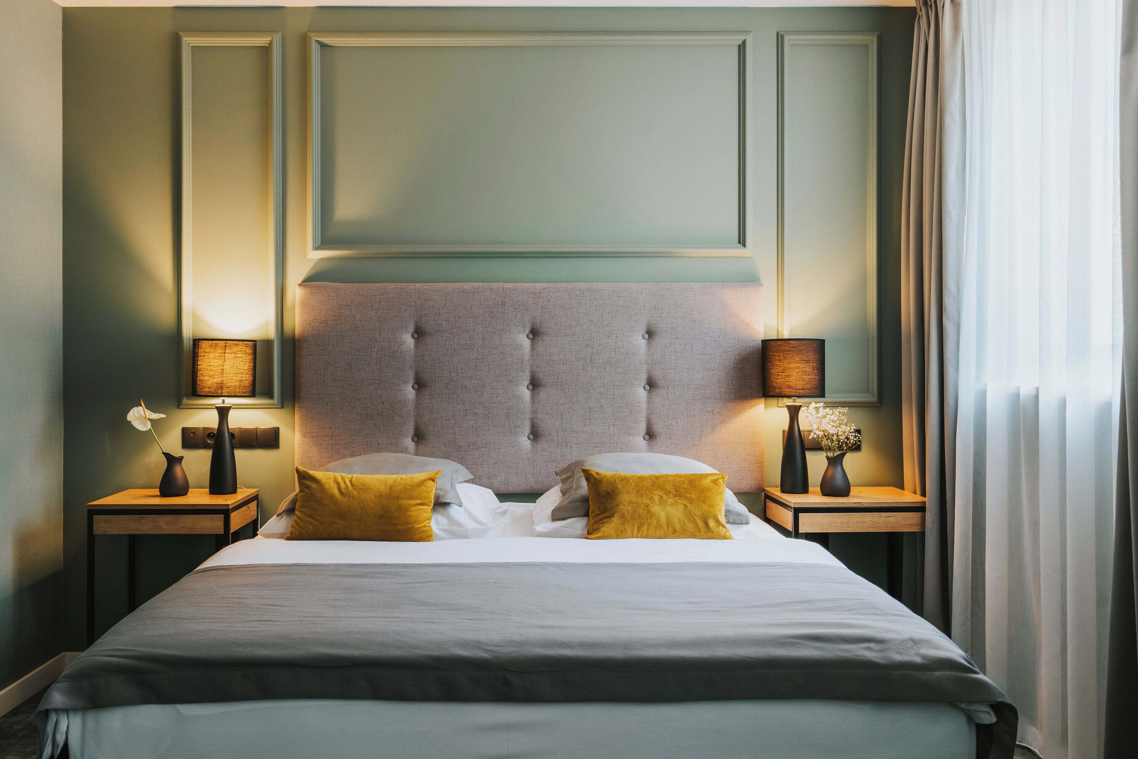 A neatly made bed with a tufted headboard, two bedside tables with lamps, and a vase with flowers on each side.