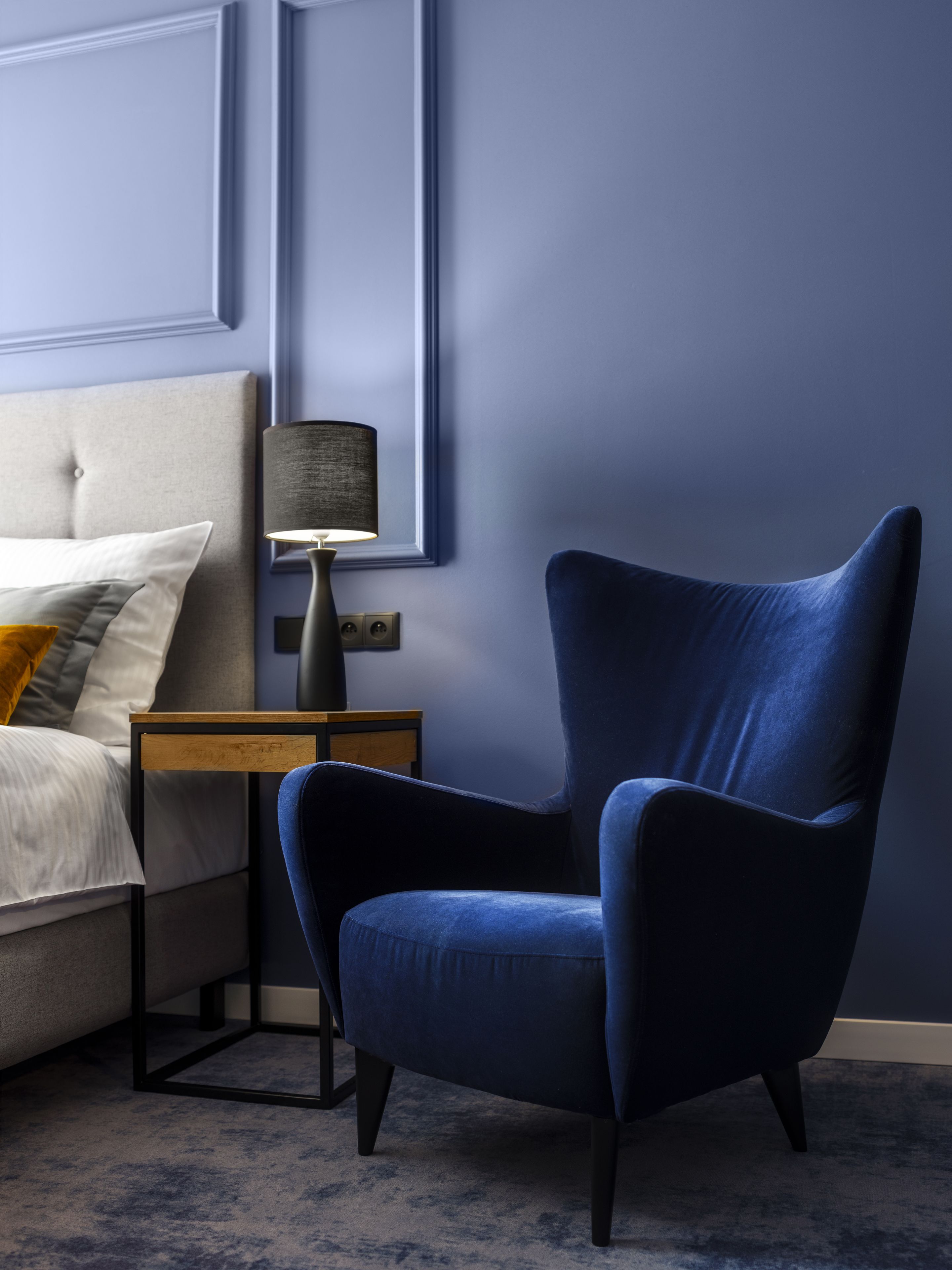 A bedroom with a bed, a nightstand, a lamp, and a blue armchair.