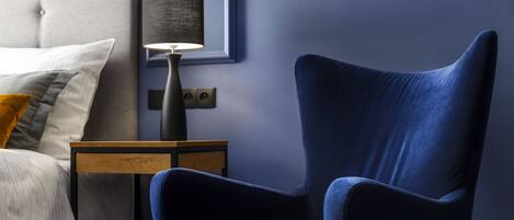 A bedroom with a bed, a nightstand, a lamp, and a blue armchair.