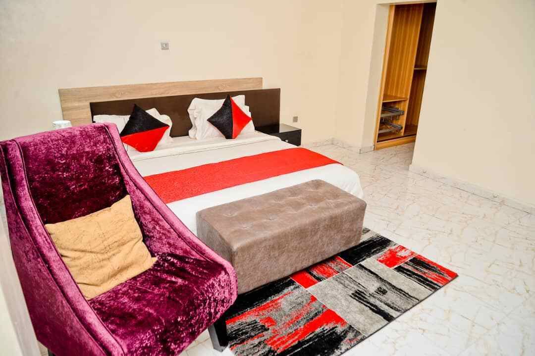 A bedroom with a bed, a nightstand, a chair, and a small ottoman.