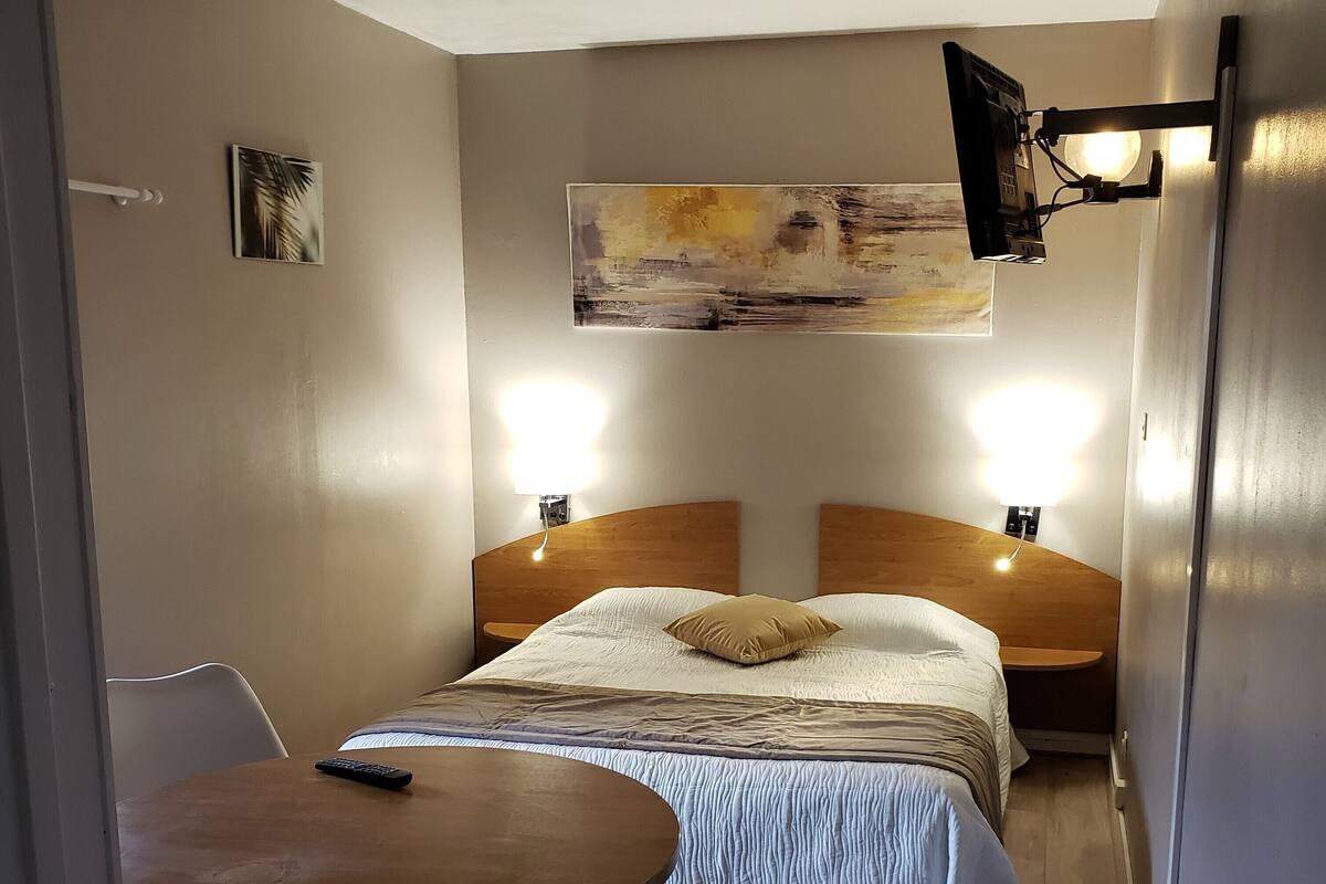 Een slaapkamer met een bed, nachtkastjes, een klein tafeltje en een stoel.