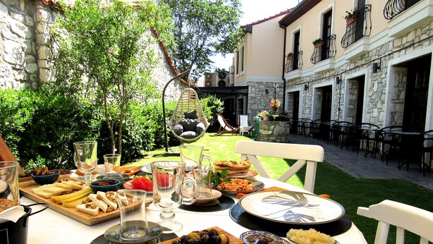 An outdoor dining area with a table set for a meal, surrounded by stone buildings and greenery. - Pintura Urla Butik Otel & Sanat Galerisi (Urla)