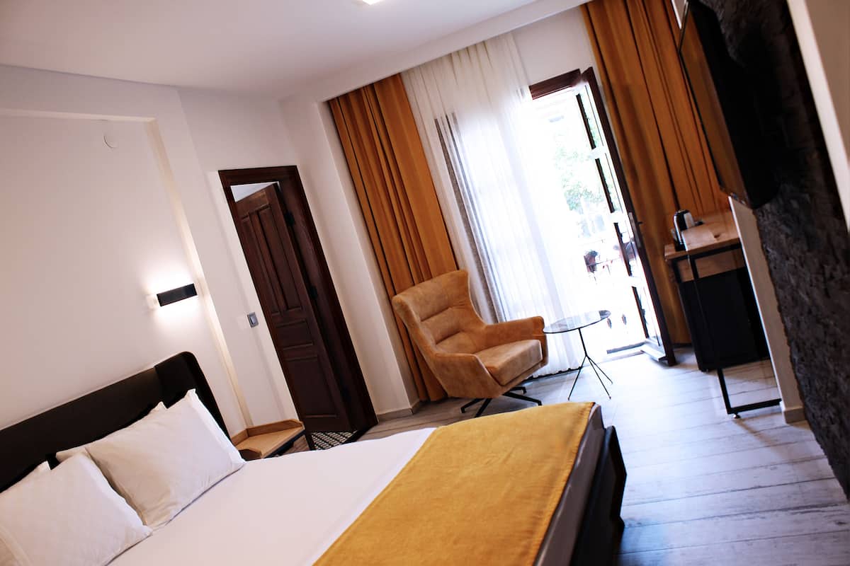 A hotel room with a bed, a chair, a desk, and a door leading to a balcony.