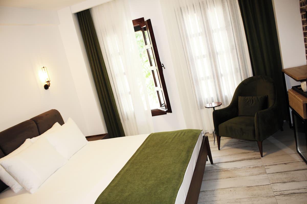 A hotel room with a bed, a chair, a desk, and a window with curtains.