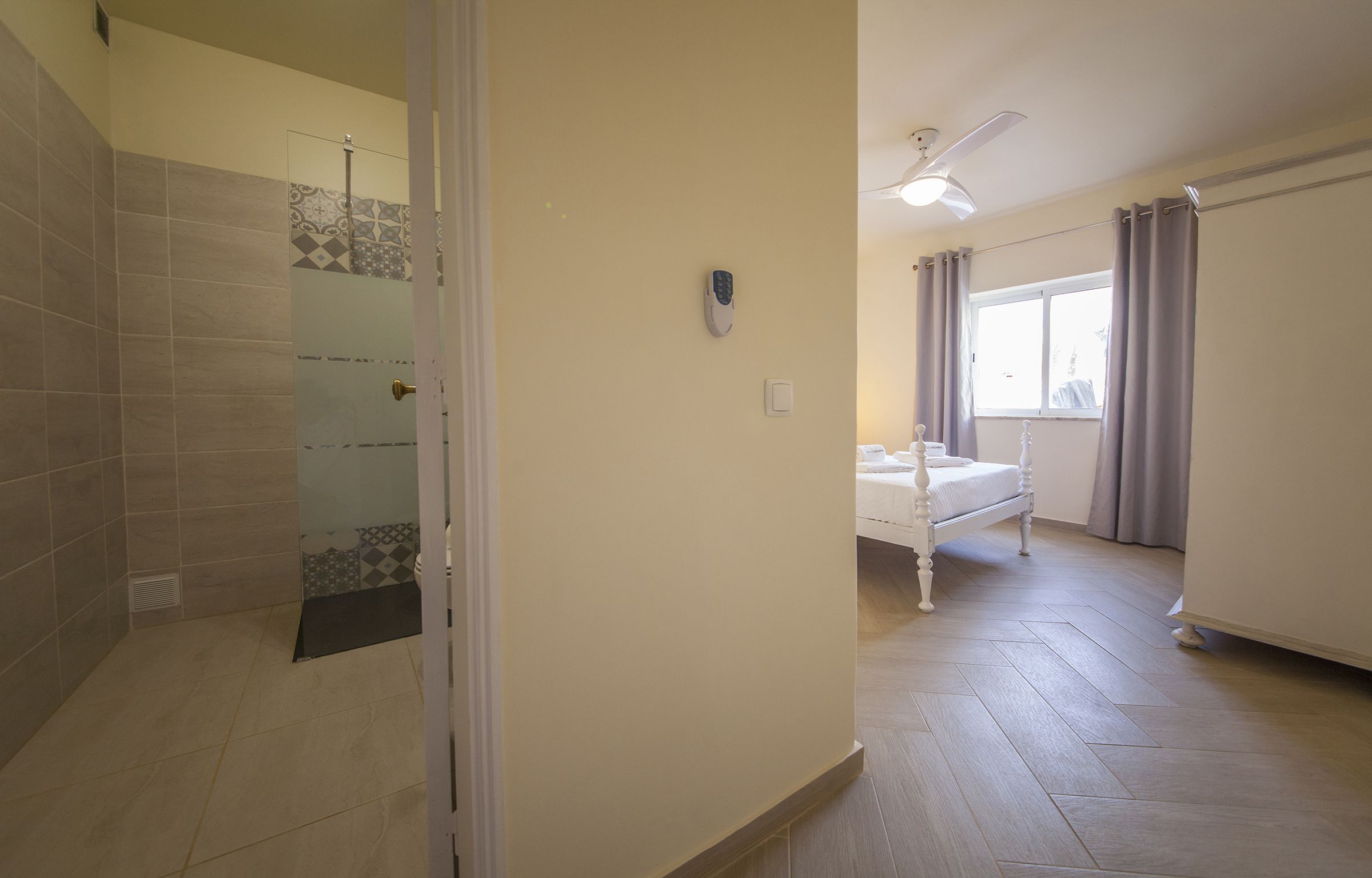 Une chambre avec une douche, un lit, un ventilateur de plafond et une fenêtre avec des rideaux.