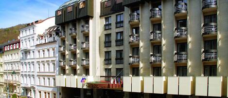 Un hotel de varios pisos con balcones, una entrada principal y un jardín ajardinado.
