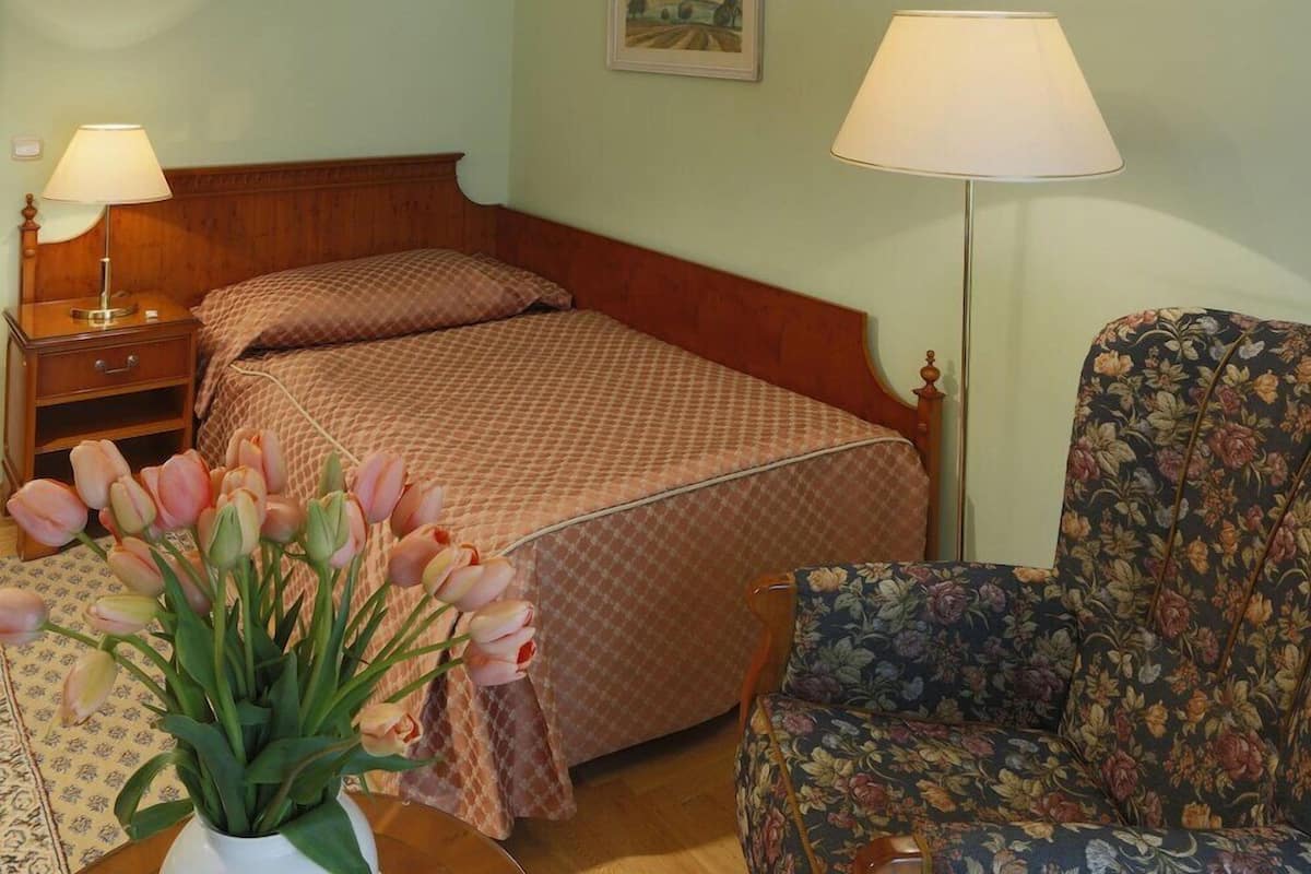 A hotel room with a bed, bedside tables, a chair, a lamp, and a vase of flowers.