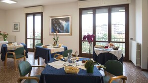 A dining area with tables set for breakfast, large windows with views, and a framed artwork on the wall. - Casa al Carmine (Padova)