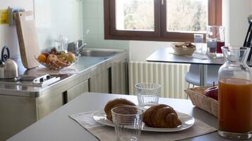Una cocina con una mesa preparada para el desayuno, incluyendo cruasanes, vasos y un frutero.