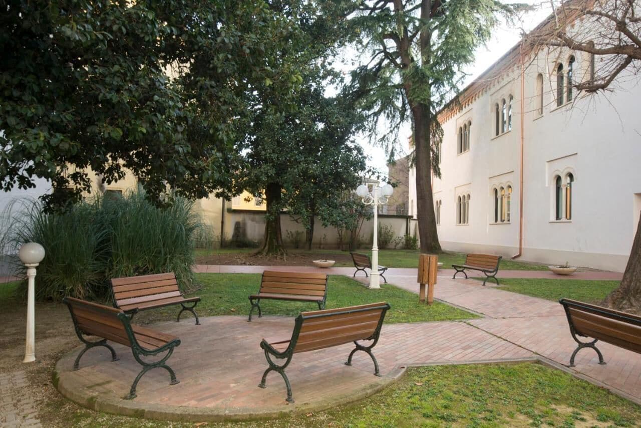 A courtyard with benches, a pathway, and a building with arched windows.