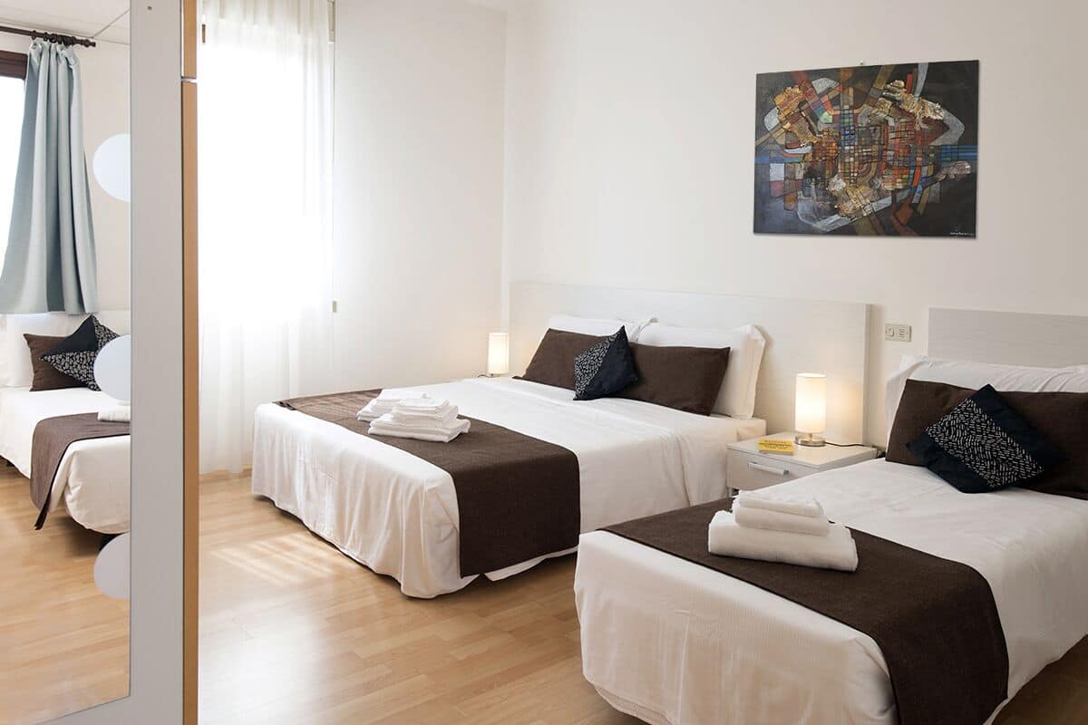 A hotel room with two beds, each with a white and brown bedspread, a nightstand with a lamp, and a painting on the wall.