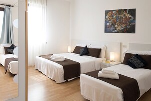 Habitación de hotel con dos camas, cada una con cubrecama blanco y marrón, una mesita de noche con lámpara y un cuadro en la pared.