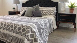 Une chambre à coucher bien rangée, avec un grand lit, deux tables de chevet, une petite table et une plante en pot.