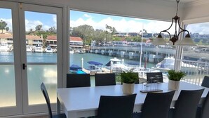 Un espace repas avec une table blanche, des chaises noires et une vue sur le port de plaisance.