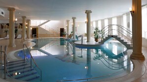 Een binnenzwembad met een centrale trap, kolommen en lounge stoelen.