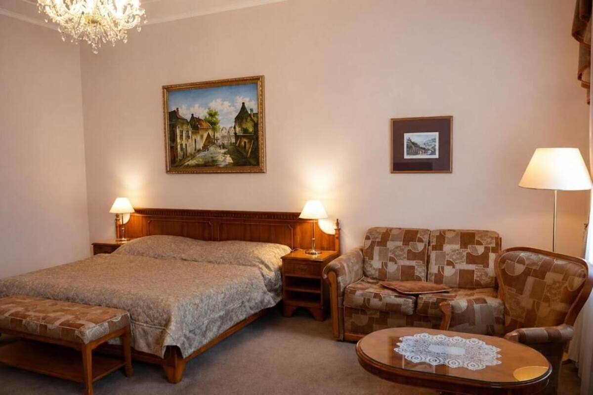 Een hotelkamer met een bed, een bank, een kleine tafel, een bankje, een kroonluchter en twee wandlampen.