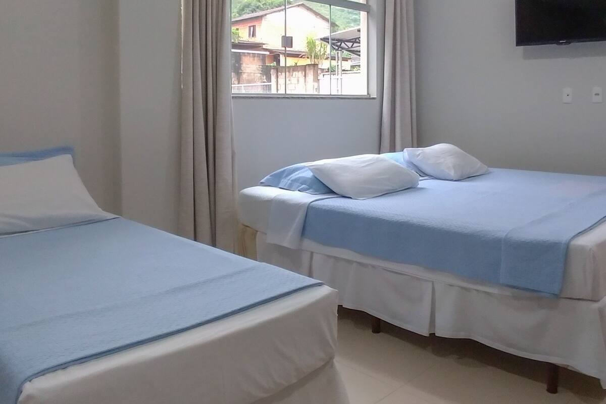 Quarto de hotel com duas camas, janela com cortinas, televisão de tela plana na parede e vista para o exterior.