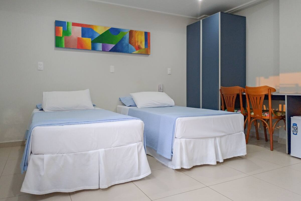 Quarto de hotel com duas camas, uma escrivaninha e uma cadeira.