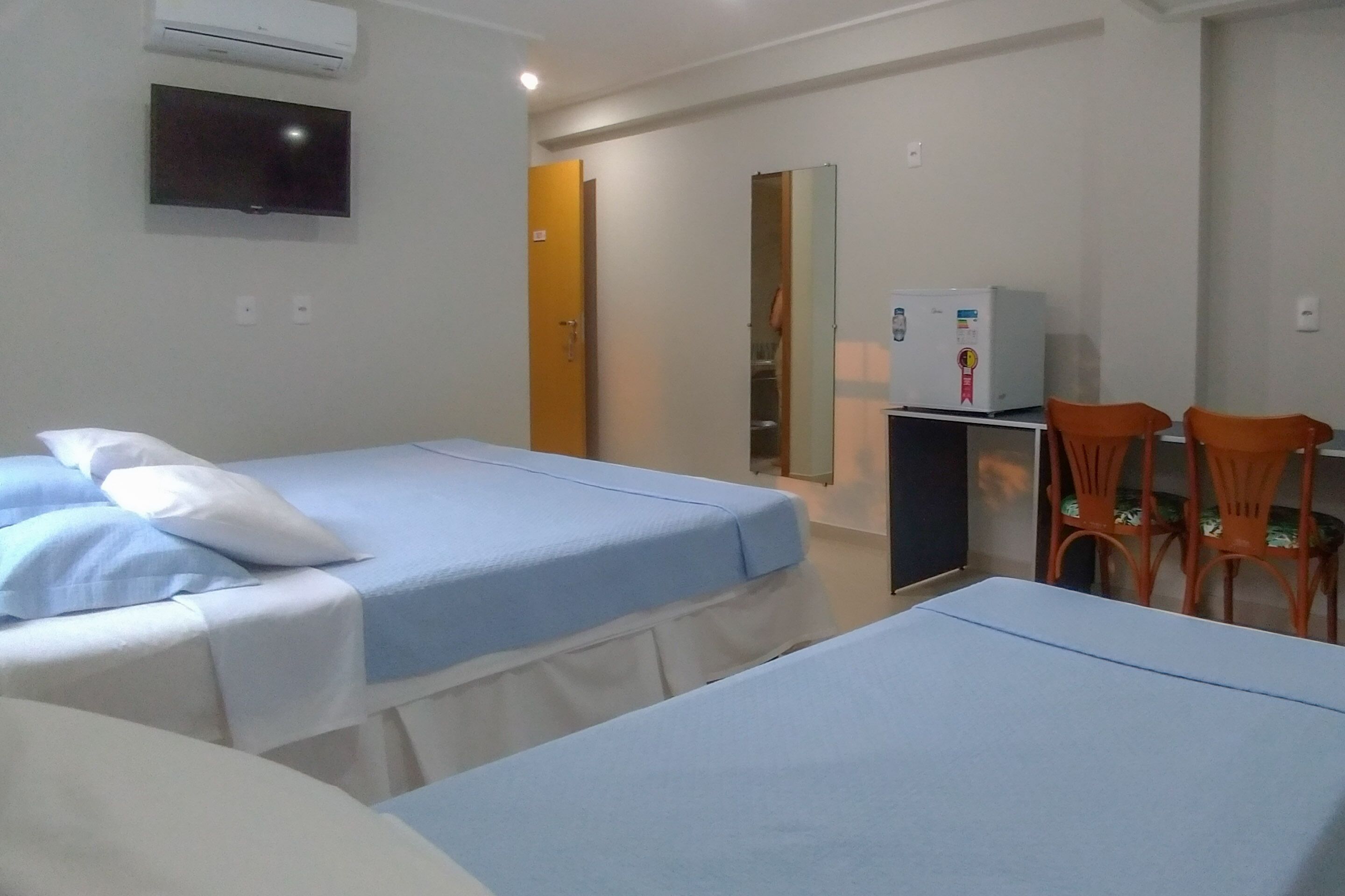 Quarto de hotel com duas camas, televisão, frigorífico e duas cadeiras.