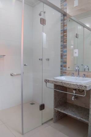 Et moderne badeværelse med en brusekabine i glas, vask med granitbordplade og et stort spejl.