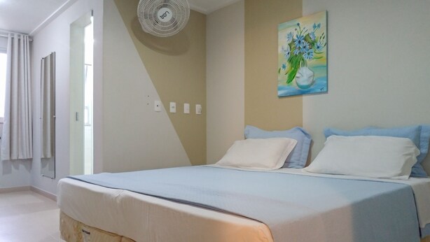 A hotel room with a large bed, a ceiling fan, a painting on the wall, and a window with curtains. - Hotel Venturim (Venda Nova Do Imigrante)