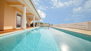 Ein klares, blaues Schwimmbecken mit weißer Brüstung, eine überdachte Terrasse mit Gartenmöbeln und Blick zum Himmel.