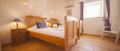 A bedroom with a wooden bed, a nightstand, a chair, and a window with curtains.