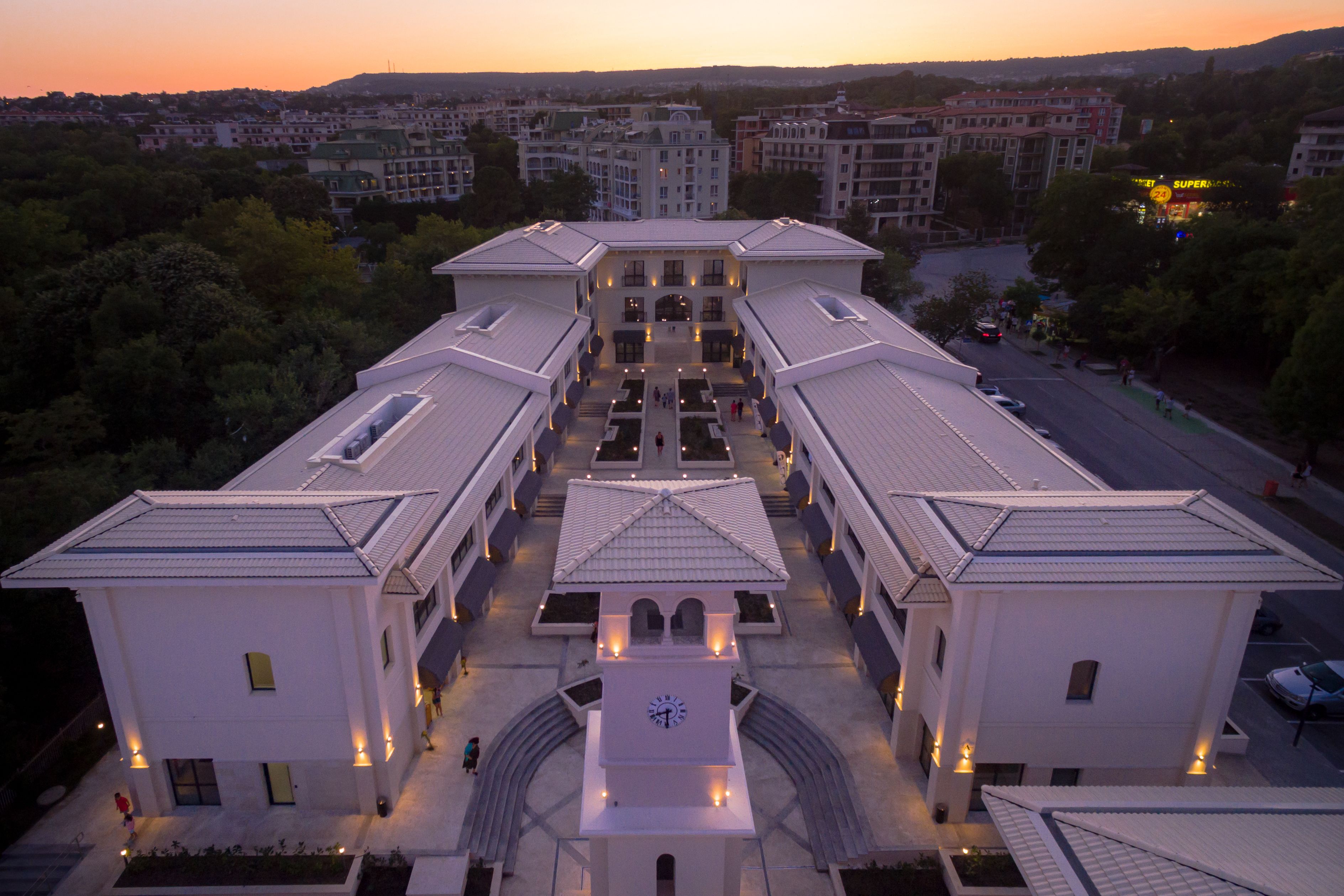 Un grand bâtiment symétrique, doté d’une tour horloge centrale, entouré de structures plus petites, qui font probablement partie d’un complexe hôtelier.