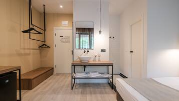 Ein modernes Hotelzimmer mit einer hölzernen Bank, einem Waschbecken mit Spiegel, einem Bett und einem kleinen Tisch.