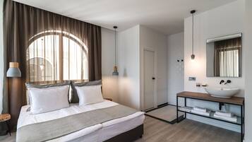Een moderne hotelkamer met een groot bed, een houten nachtkastje, een ingebouwd wastafeltje en een grote spiegel.