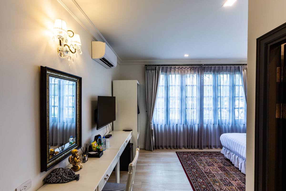 Hotellihuone, jossa on suuri sänky, televisio, peilillä varustettu työpöytä ja ikkuna, jossa on verhot.