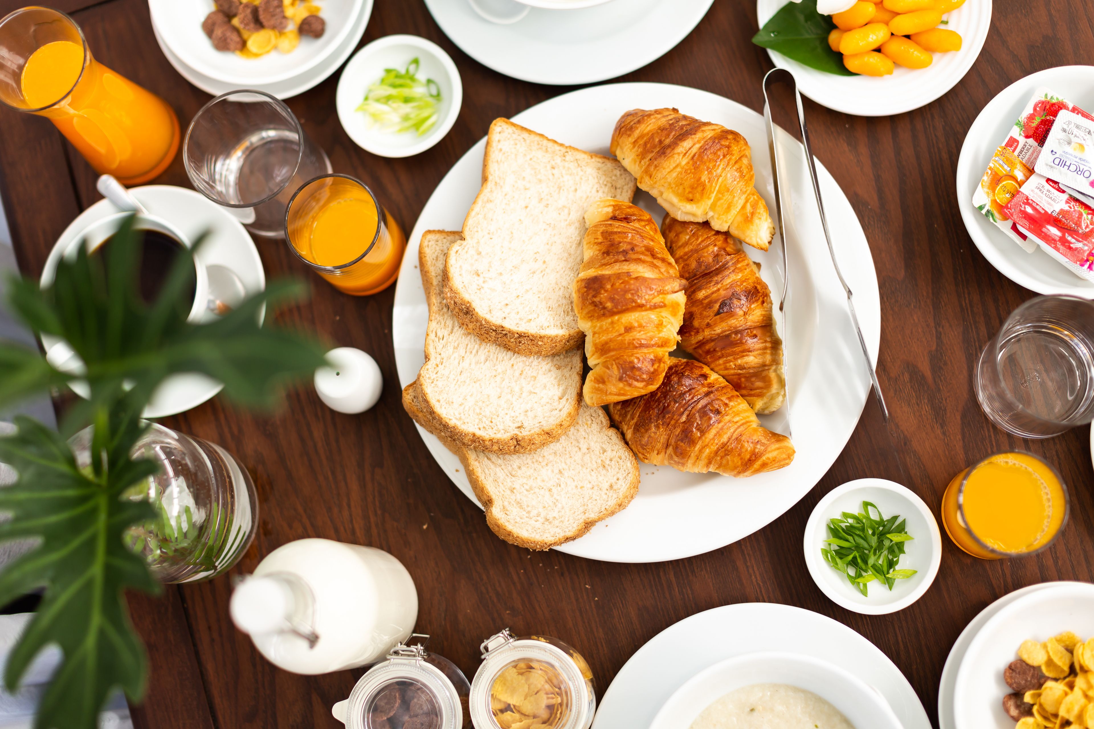 A breakfast setting with croissants, toast, and orange juice on a wooden table.