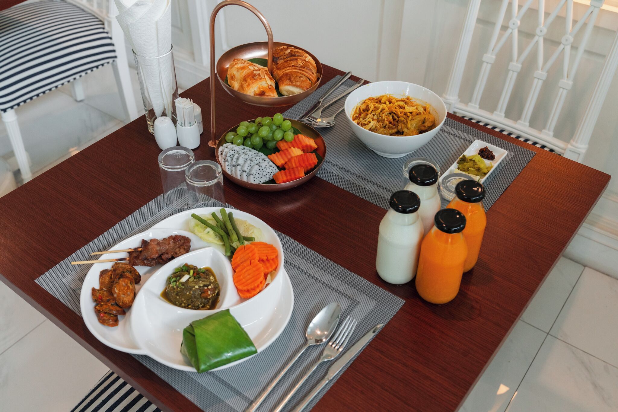 Ein Esstisch mit verschiedenen Speisen, darunter eine Nudelschüssel, ein Teller mit Fleisch und Gemüse sowie eine Platte mit Croissants.
