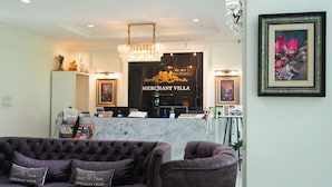 Uma área de recepção com balcão de mármore, um candelabro e um sofá com almofadas com a inscrição 'Merchant Villa'.