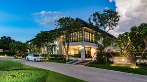 Uma villa moderna com uma entrada bem iluminada, um acesso por carro e uma placa com a inscrição 'MERCHANT VILLA'.